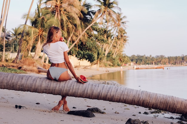 Młoda kobieta pasuje z arbuzem na tropikalnej plaży o zachodzie słońca