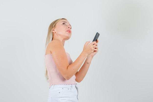 Młoda kobieta, patrząc na bok, trzymając smartfon w podkoszulku