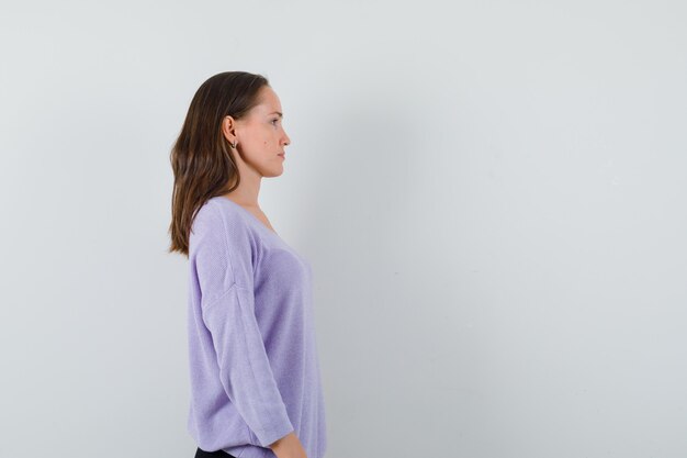 Młoda kobieta patrząc na bok w liliowej bluzce i wyglądająca spokojnie. miejsce na tekst