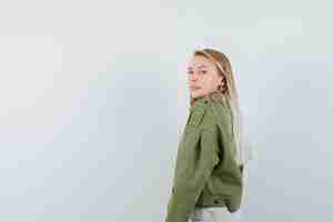 Bezpłatne zdjęcie młoda kobieta, patrząc przez ramię w zielonej kurtce, dżinsach i rozsądnie wyglądającej. . miejsce na tekst