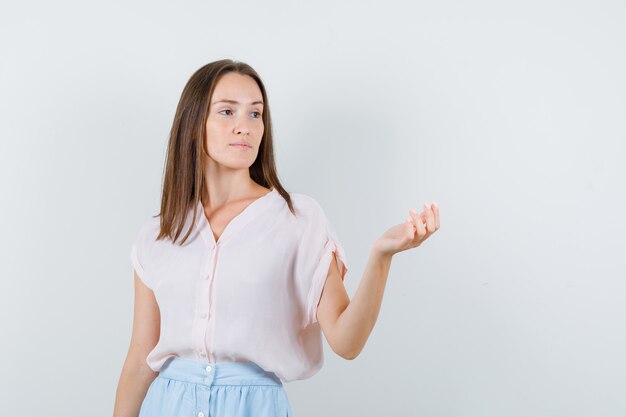 Młoda kobieta, patrząc z podniesioną dłonią w t-shirt, spódnicę i zamyślony widok z przodu.