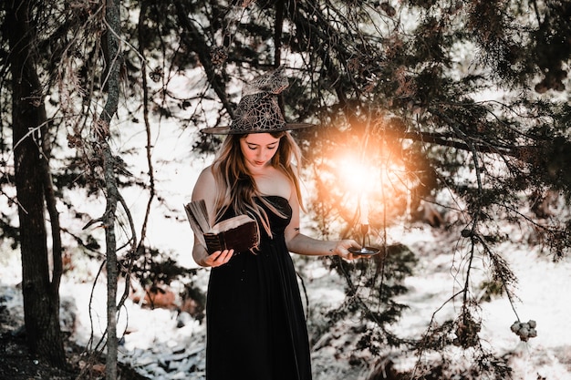 Bezpłatne zdjęcie młoda kobieta patrzeje w dół w lesie z książką i świeczką