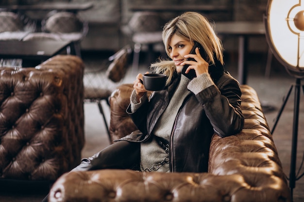 Młoda kobieta pije kawę i rozmawia przez telefon w kawiarni