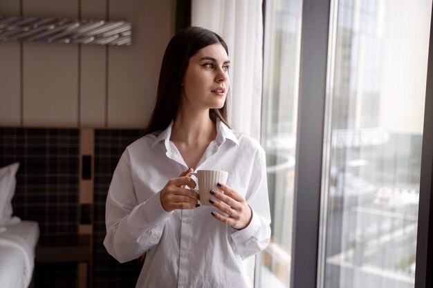Młoda kobieta pije kawę w pokoju hotelowym