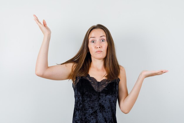 Młoda kobieta pokazująca bezradny gest w czarnym podkoszulku i wyglądająca na zdezorientowaną.