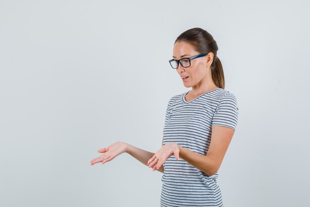 Młoda kobieta pokazuje dłonie w t-shirt w paski, okulary i wygląda na zdumionego. przedni widok.