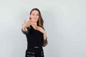 Bezpłatne zdjęcie młoda kobieta pozuje, jakby pokazywała swój pierścionek w czarnej bluzce i wyglądała na zadowoloną