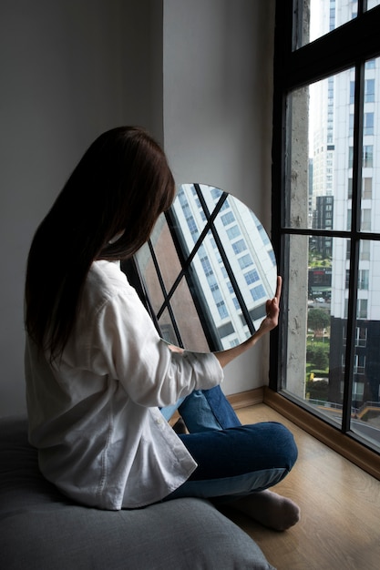 Bezpłatne zdjęcie młoda kobieta pozuje obok lustra tworząc odbicie