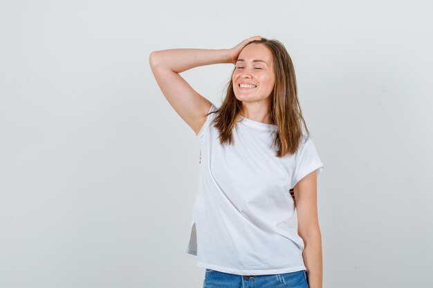 Młoda Kobieta Pozuje Z Ręką Na Głowie W Biały T-shirt, Spodenki I Patrząc Wesoło. Przedni Widok.