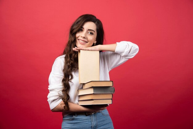 Młoda kobieta prowadzenia książek i uśmiecha się na czerwonym tle. Zdjęcie wysokiej jakości