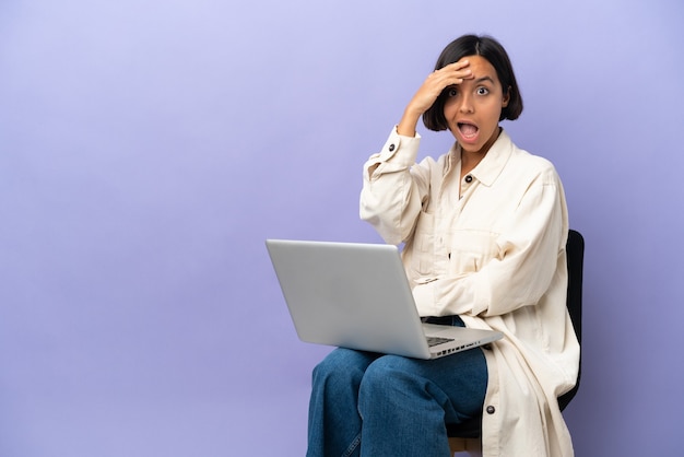 Młoda kobieta rasy mieszanej siedząca na krześle z laptopem na fioletowym tle uświadomiła sobie coś i zamierza znaleźć rozwiązanie