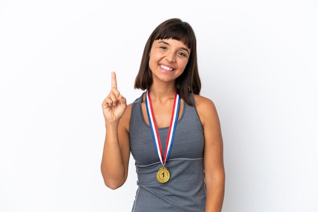 Młoda kobieta rasy mieszanej z medalami na białym tle pokazująca i unosząca palec na znak najlepszych