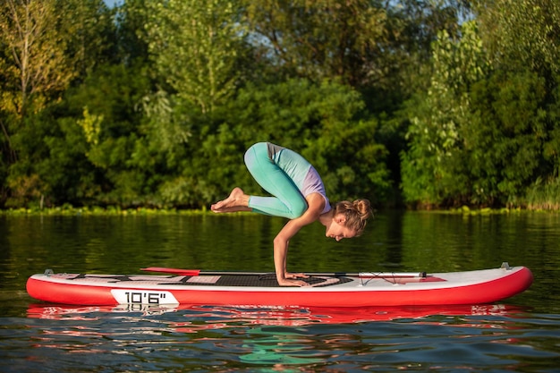Młoda kobieta robi jogę na stojącej desce SUP na pięknym jeziorze lub rzece. Pojęcie zdrowego stylu życia. Sport. Joga. Hobby