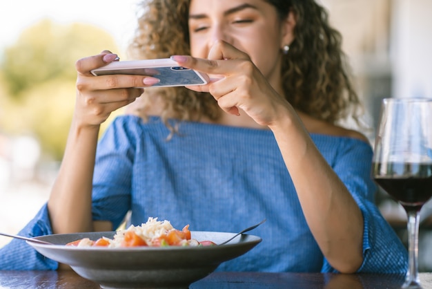Młoda kobieta robienie zdjęć do jedzenia podczas obiadu w restauracji.