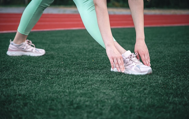 Młoda kobieta rozciąga się przed joggingiem siedząc na stadionie