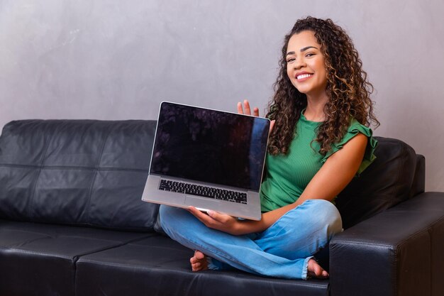 Młoda kobieta siedzi na kanapie posiadania komputera typu laptop pc z pustym pustym ekranem z miejscem na tekst.