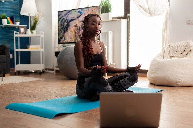 Młoda kobieta siedzi na macie do jogi, ćwicząc spokojną harmonię, medytując zen dla zdrowego stylu życia, relaksując się w pozycji lotosu