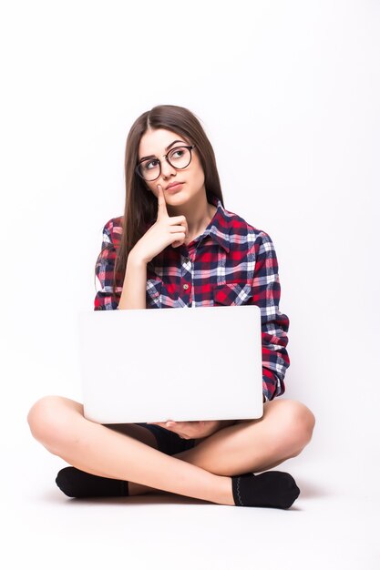 Młoda kobieta siedzi na podłodze z laptopem na białym tle