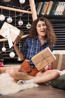 Młoda kobieta siedzi na puszystym dywanie z pudełkami świątecznych prezentów