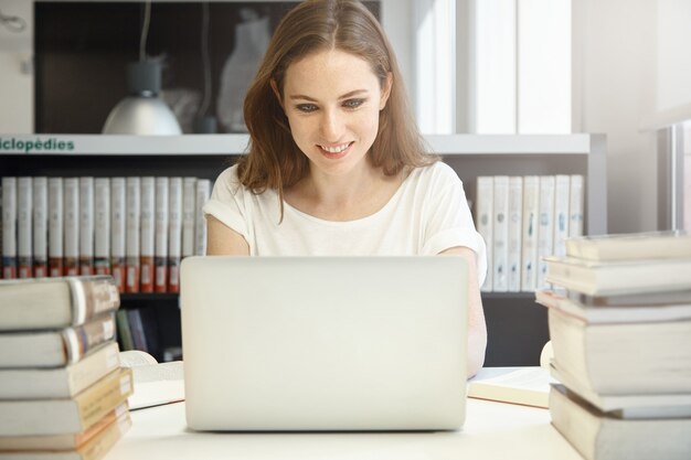 Młoda kobieta siedzi w bibliotece z laptopem