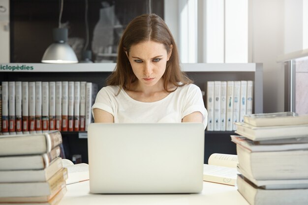 Młoda kobieta siedzi w bibliotece z laptopem