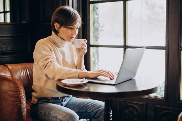 Młoda kobieta siedzi w kawiarni, pije kawę i pracuje na komputerze