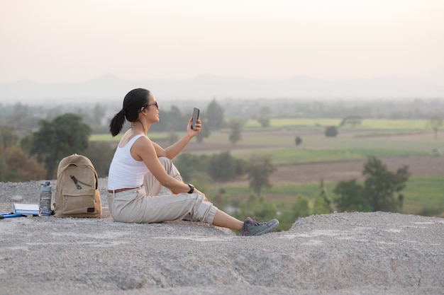 Młoda kobieta siedzi z telefonem komórkowym. Szlak turystyczny w wysokich górach o zachodzie słońca.
