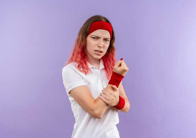 Młoda kobieta sportowy źle wyglądający dotykając jej rękę, czując ból stojąc nad fioletową ścianą