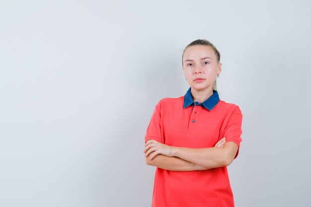 Młoda kobieta stojąca ze skrzyżowanymi rękami w t-shirt i wyglądająca rozsądnie. przedni widok.