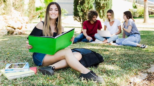Młoda kobieta studiuje obsiadanie na trawie blisko uniwersyteta