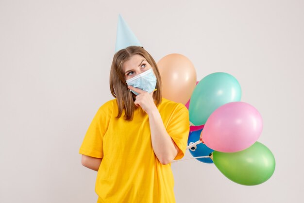 młoda kobieta trzyma kolorowe balony w masce myśli na białym tle