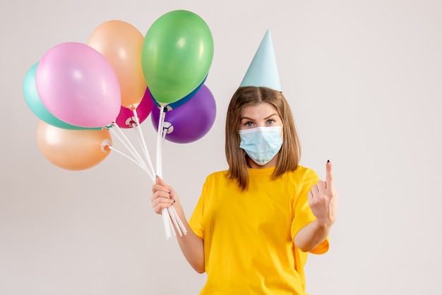 młoda kobieta trzyma kolorowe balony w sterylnej masce na białym tle
