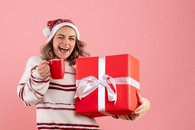młoda kobieta trzyma prezent świąteczny i filiżankę herbaty na różowo