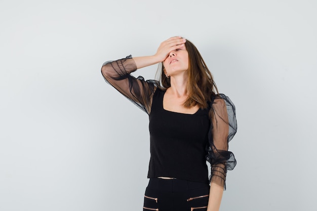 Młoda kobieta trzyma rękę na głowie w czarnej bluzce i wygląda na wyczerpaną. przedni widok.