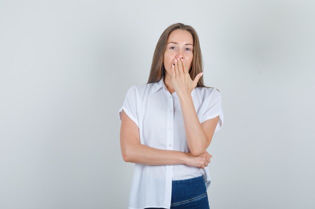 Młoda kobieta trzyma rękę na ustach w t-shirt, dżinsy i patrząc zaskoczony