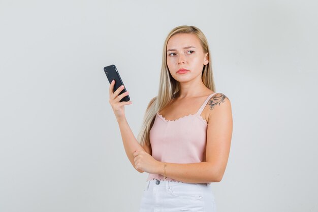 Młoda kobieta trzyma smartfon, patrząc z boku w podkoszulek