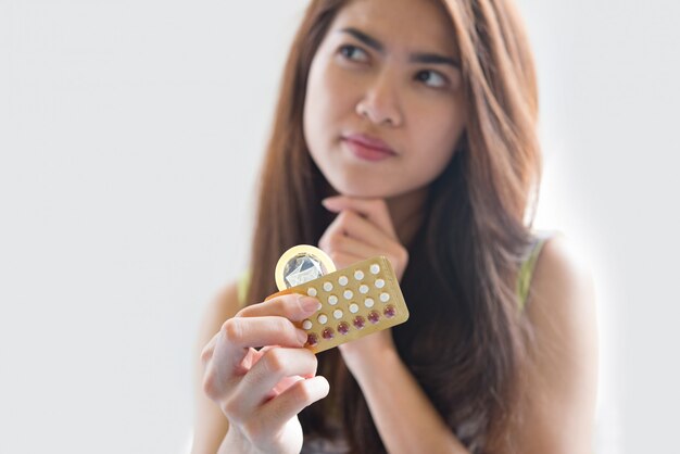 Młoda kobieta trzymając prezerwatywę i pigułki antykoncepcyjne zapobiegają ciąży