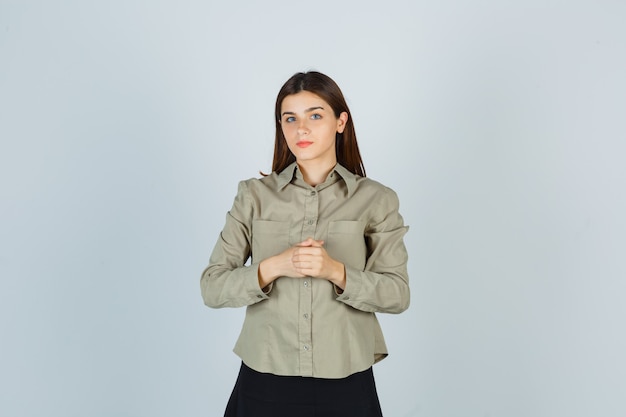 Bezpłatne zdjęcie młoda kobieta trzymając ręce na klatce piersiowej w koszuli, spódnicy i wyglądającej rozsądnie
