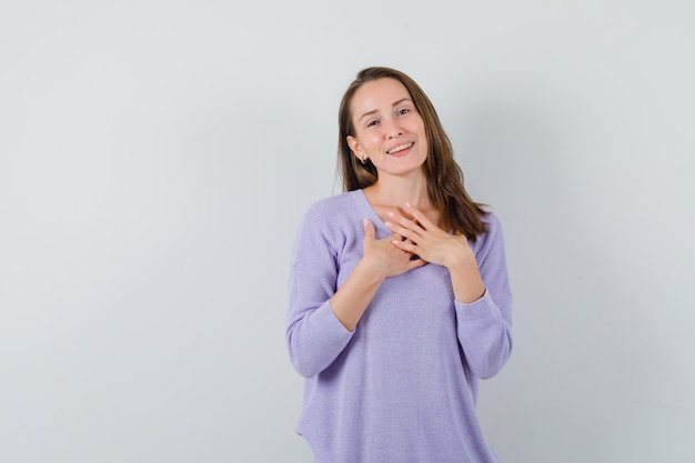 Młoda kobieta trzymając rękę na jej piersi w liliowej bluzce i patrząc z nadzieją. przedni widok. miejsce na tekst