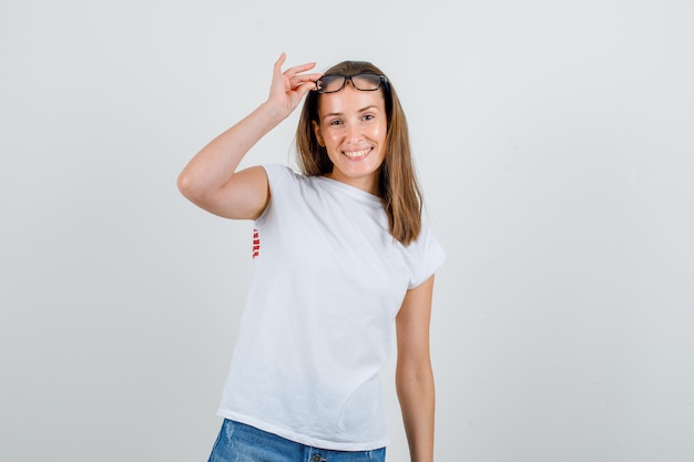 Młoda kobieta trzymając rękę na okulary w t-shirt, spodenki i patrząc wesoło. przedni widok.