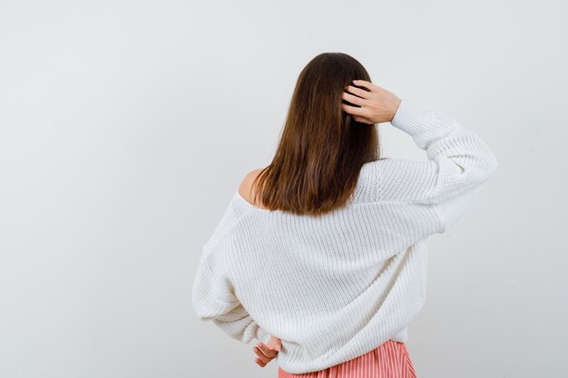 Młoda kobieta trzymając rękę za głową w sweter i spódnicę patrząc zamyślony na białym tle