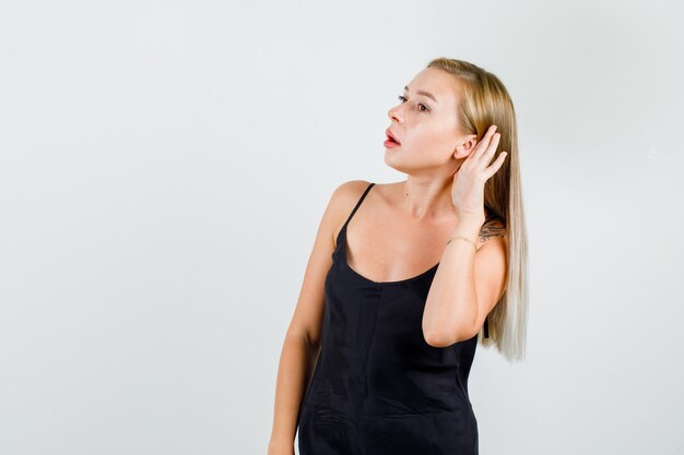 Młoda kobieta trzymając rękę za ucho, aby usłyszeć w czarnym podkoszulku
