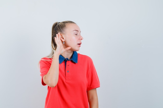 Młoda kobieta trzymając rękę za ucho w t-shirt i patrząc zaciekawiony