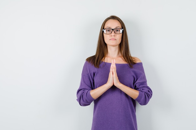 Bezpłatne zdjęcie młoda kobieta trzymając się za ręce w geście modlitwy w fioletowej koszuli i patrząc spokojny, przedni widok.