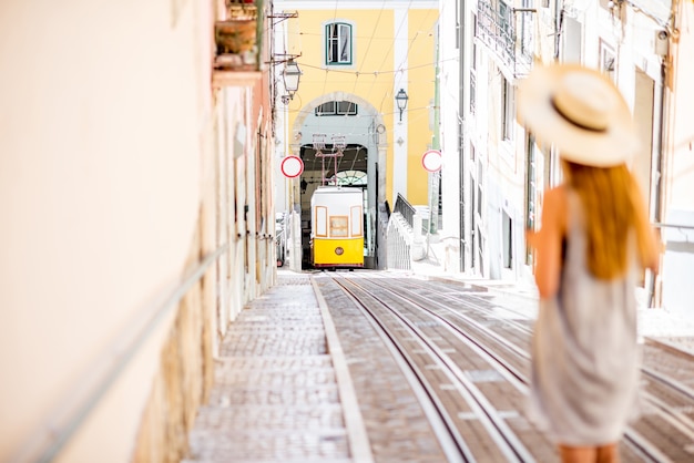Młoda kobieta turysta patrząc na słynny retro żółty tramwaj na ulicy w mieście lizbona, portugalia. kobieta jest nieostra