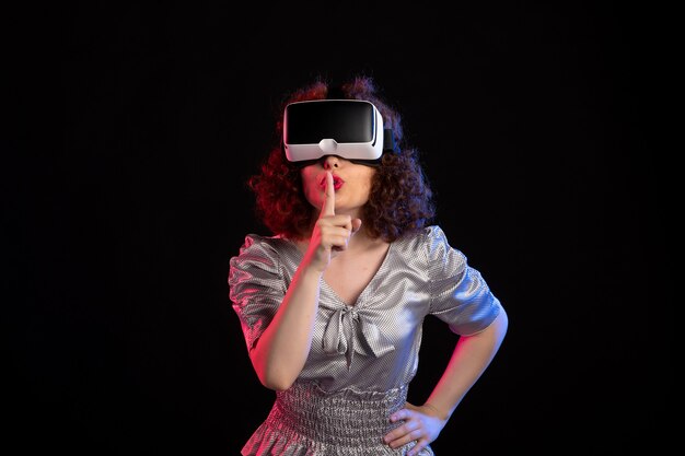 Młoda kobieta ubrana w zestaw słuchawkowy wirtualnej rzeczywistości na ciemnej powierzchni