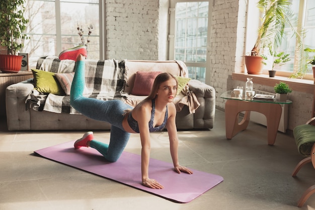 Młoda Kobieta Uczy W Domu Internetowych Kursów Fitness, Aerobiku, Sportowego Stylu życia Podczas Kwarantanny. Aktywność W Izolacji, Wellness, Koncepcja Ruchu. Trening Dolnej Części Ciała, Stretching.