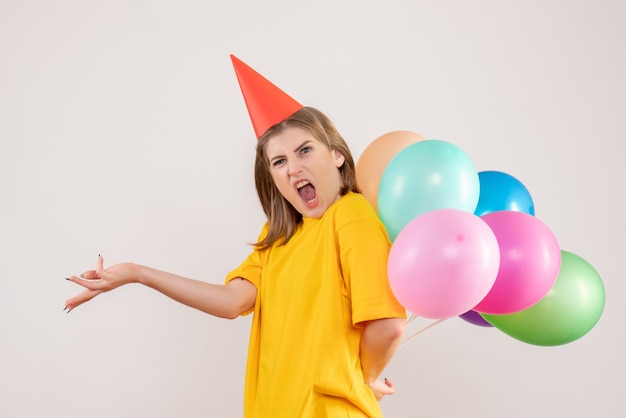 młoda kobieta ukrywa kolorowe balony za plecami na białym tle