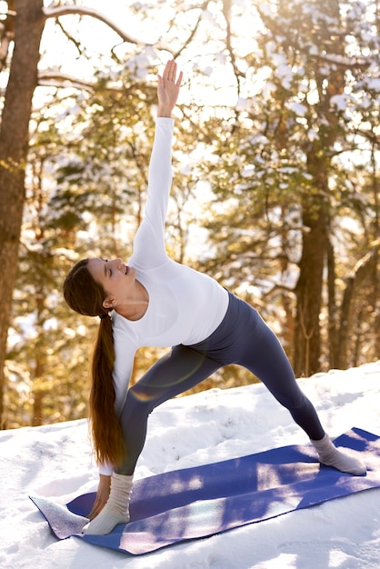 Bezpłatne zdjęcie młoda kobieta uprawiająca jogę na świeżym powietrzu zimą w otoczeniu drzew