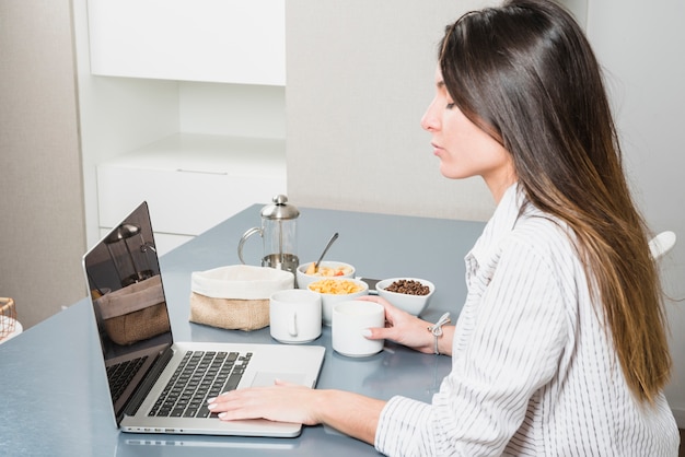 Młoda kobieta używa laptop przy śniadaniowym stołem